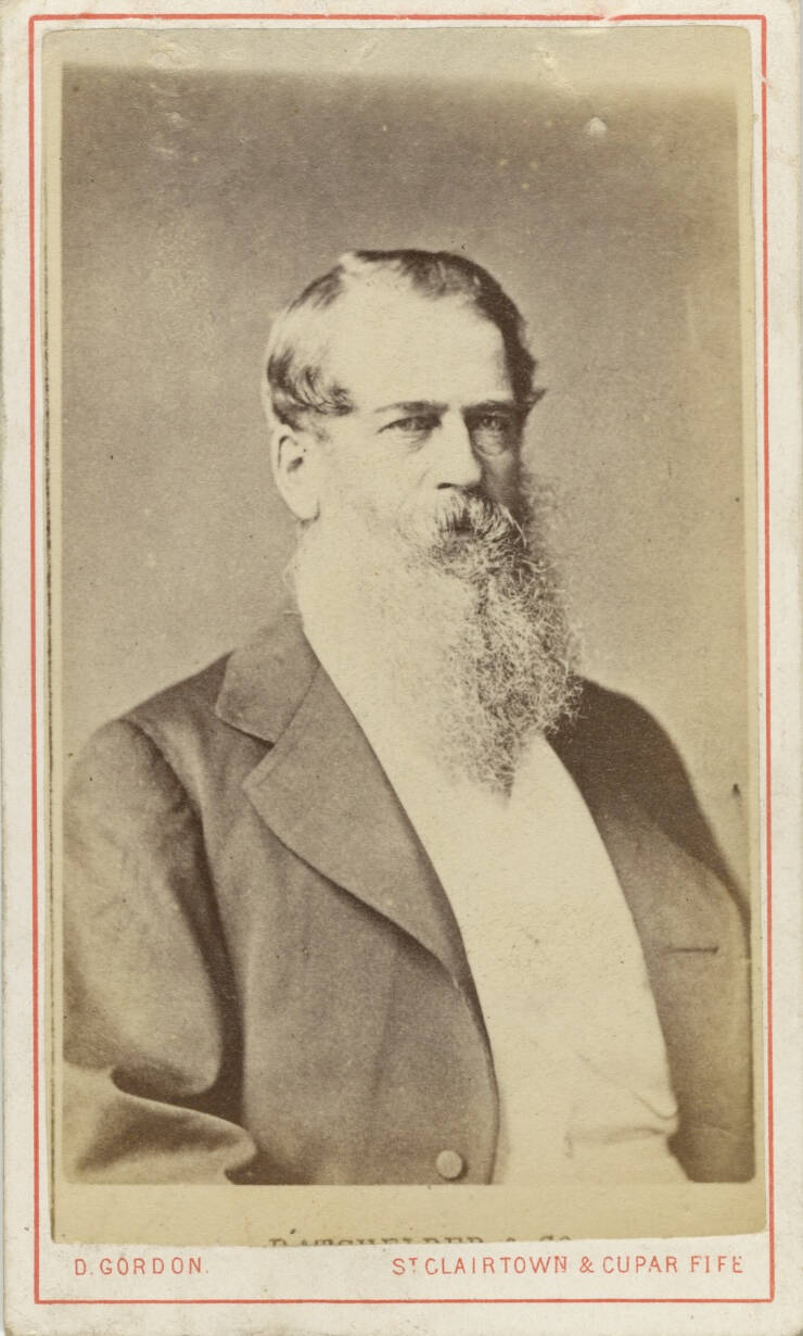 HIstoric studio portrait photograph of a seated man with an open jack and a long beard and mustache.